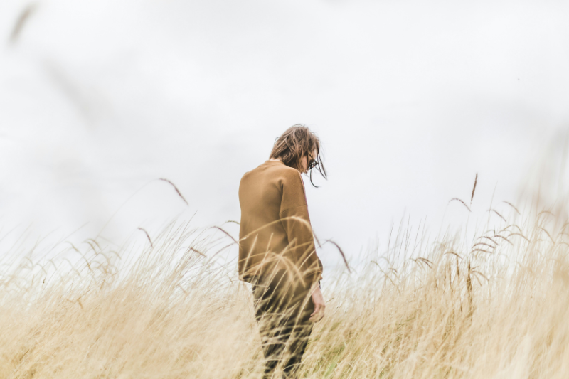 Woman standing a field of long yellow grass looking down, perhaps considering regrets